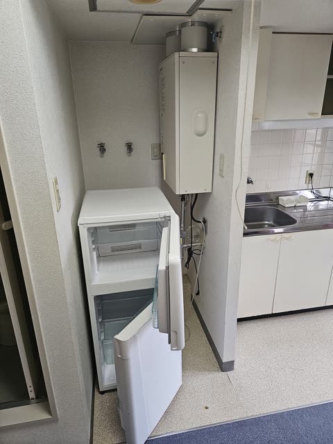 An empty white refrigerator with its doors open sits in a narrow kitchen alcove next to a sink.