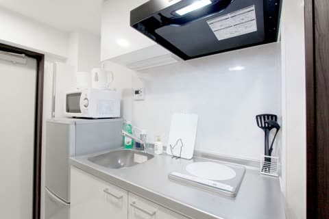A compact kitchenette features a stainless steel countertop with a sink, a small refrigerator, a microwave, and an electric kettle.