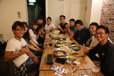 A group of people smiles and makes hand gestures for a photo while sitting at a long wooden table in a restaurant.