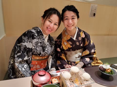 Two women in kimonos seated at a table, smiling.