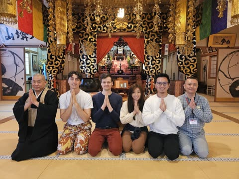 Six people kneel, hands pressed together, inside a temple.