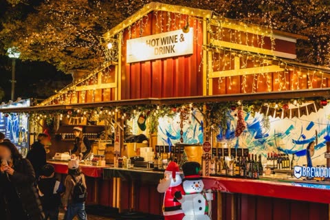 Person serving drinks at a nighttime holiday market stand.