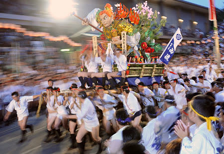 Men pulling large decorated float during nighttime festival.