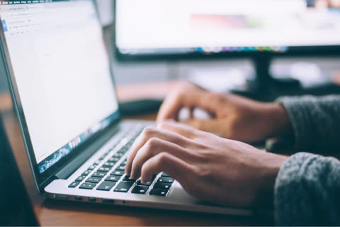 Person's hands typing on laptop keyboard at desk.
