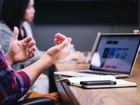 Person gesturing with hands at a table with a laptop.