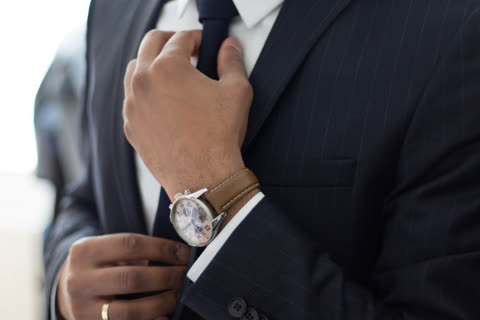 Person adjusts necktie while wearing a suit and watch.