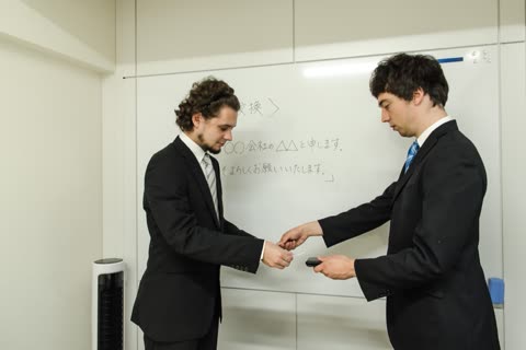 Two businessmen exchange cards in front of a whiteboard.