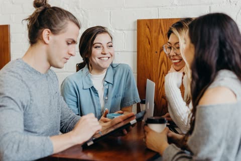 Four people use laptops and tablets at a cafe table.